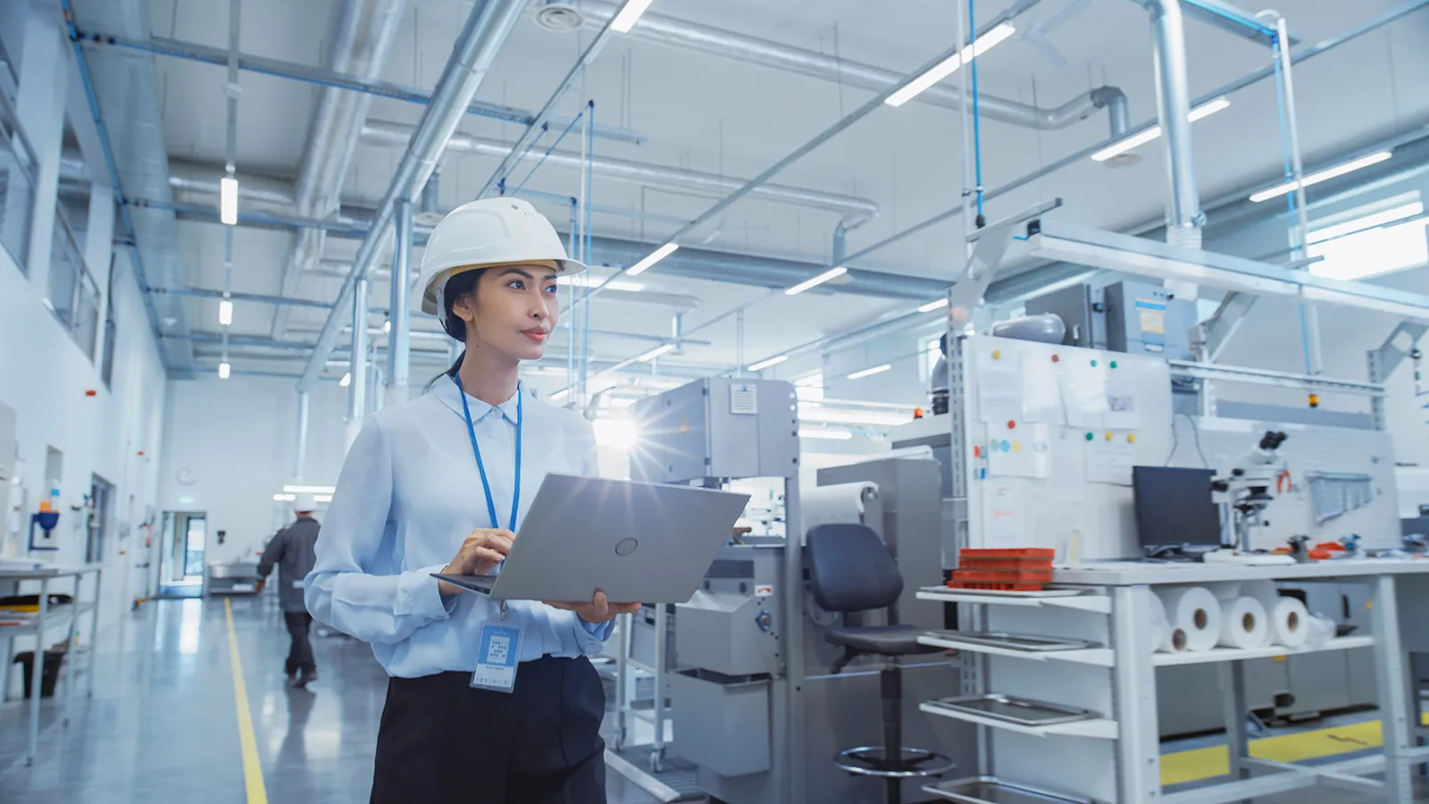 Ritratto di un ingegnere asiatico con cappello rigido che cammina e utilizza un computer portatile in una fabbrica di produzione elettronica. Tecnico al lavoro su compiti quotidiani e dati di ricerca e sviluppo.