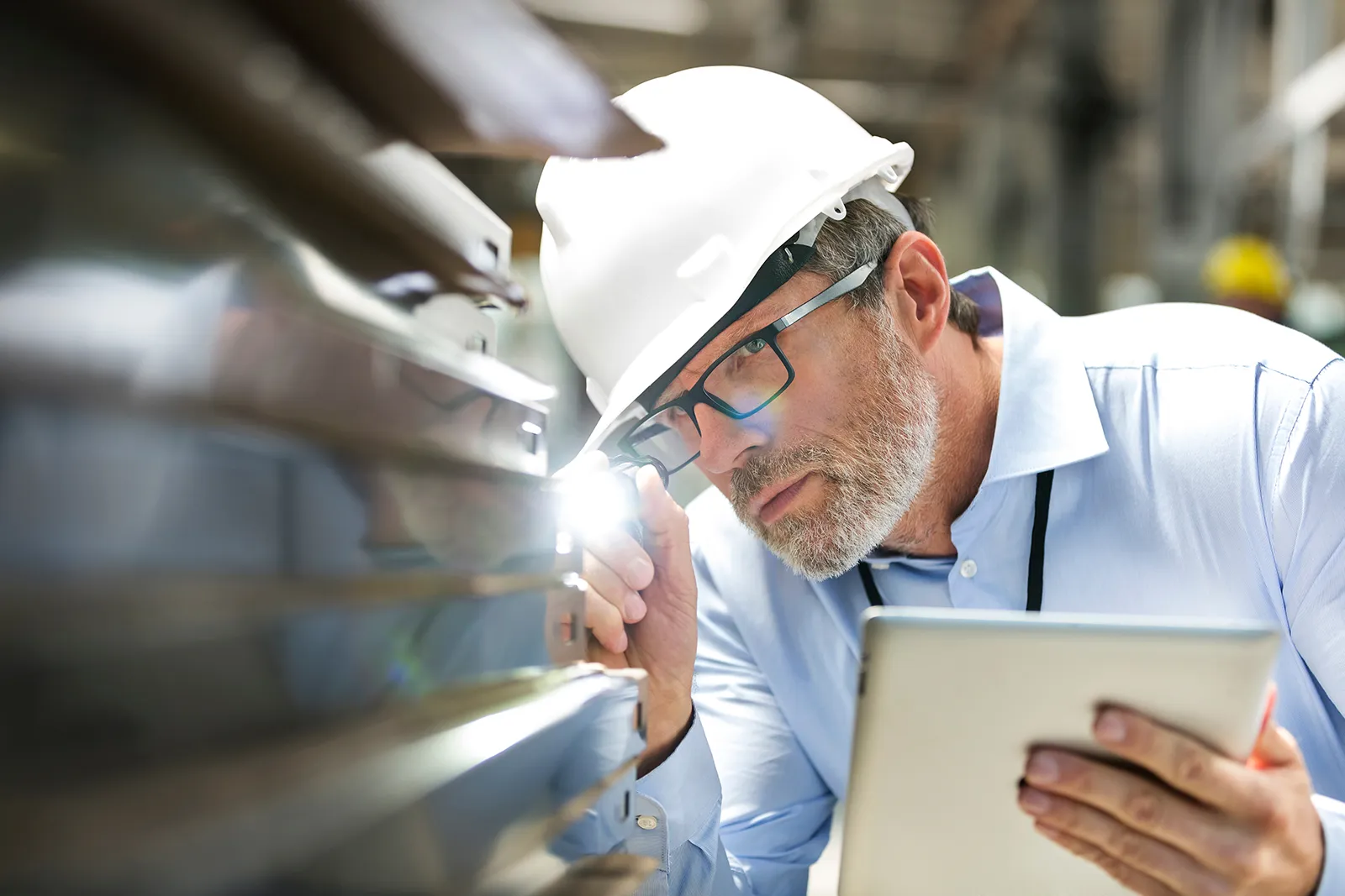 Fokussierter Ingenieur mit digitaler Tablet-Taschenlampe bei der Prüfung eines Teils in der Fabrik