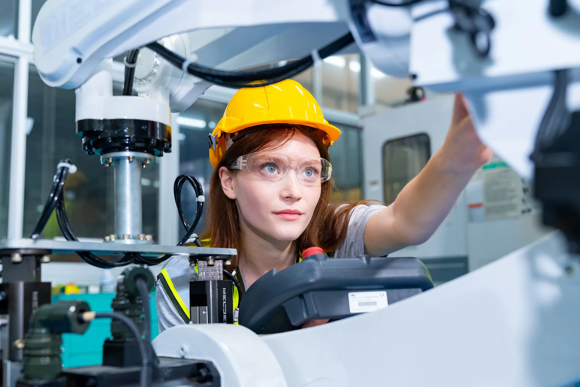 Technicienne professionnelle en vêtements de sécurité contrôlant le système de bras robotisé d'une ligne de production en vue de sa réparation et de son entretien.